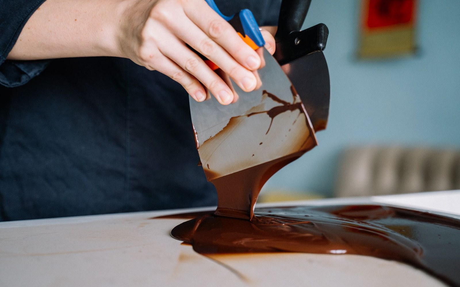 An adult pastry cook's hands working tempered chocolate across a marble slab with a metal scraper